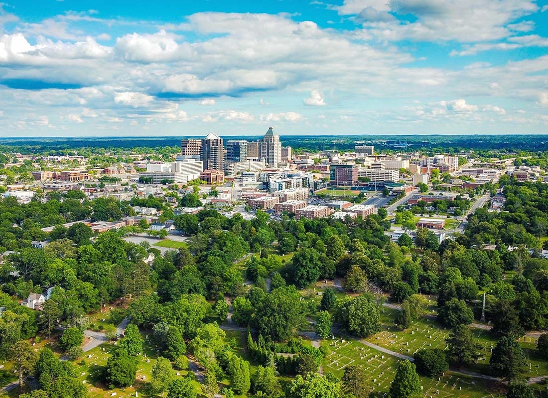 Contact - Aerial View of the City of Greensboro North Carolina Surrounded by Green Trees on a Sunny Day